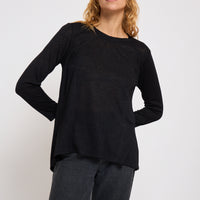 Woman wearing a black long-sleeve top and gray pants on a white background