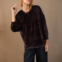 Person wearing a dark brown velvet top and black pants against a beige background