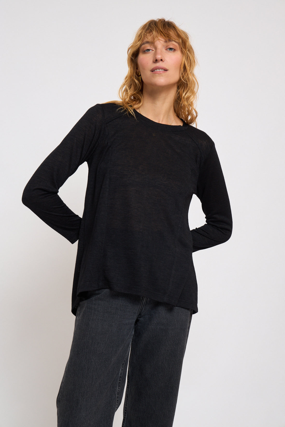 Woman wearing a black long-sleeve top and gray pants on a white background