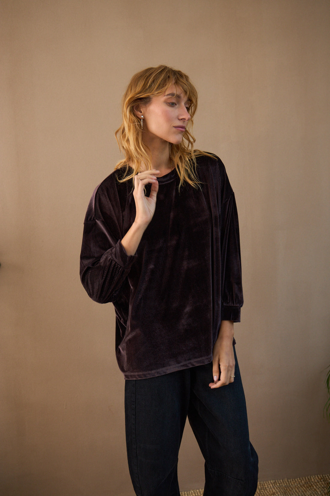 Woman wearing a dark brown velvet top and black pants against a beige background
