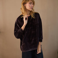 Woman wearing a dark brown velvet top and black pants against a beige background