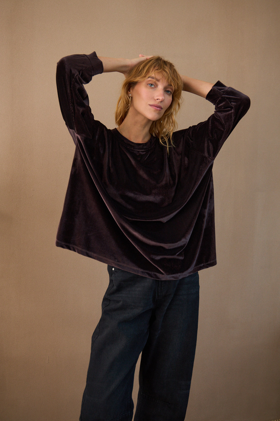 Woman wearing a dark brown velvet top and black pants against a beige background