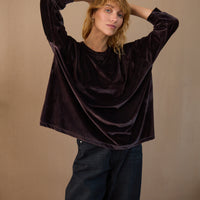 Woman wearing a dark brown velvet top and black pants against a beige background