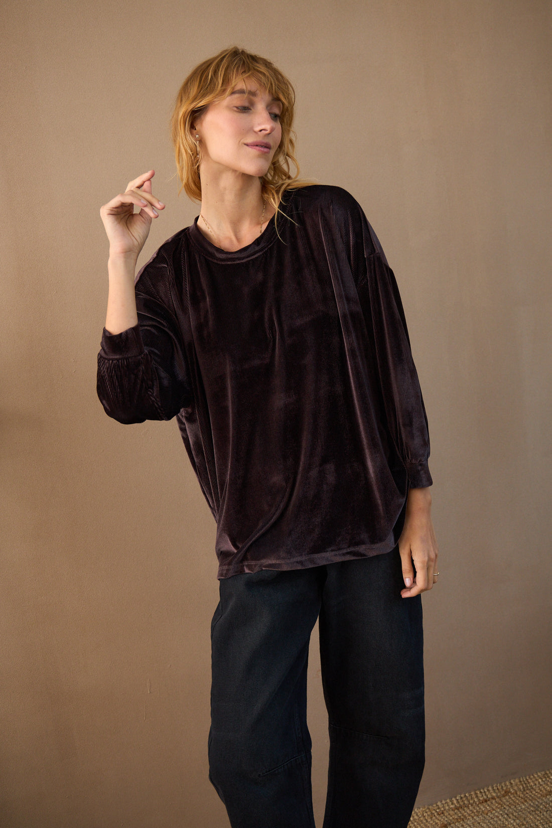 Person wearing a dark brown velvet top and black pants against a beige background